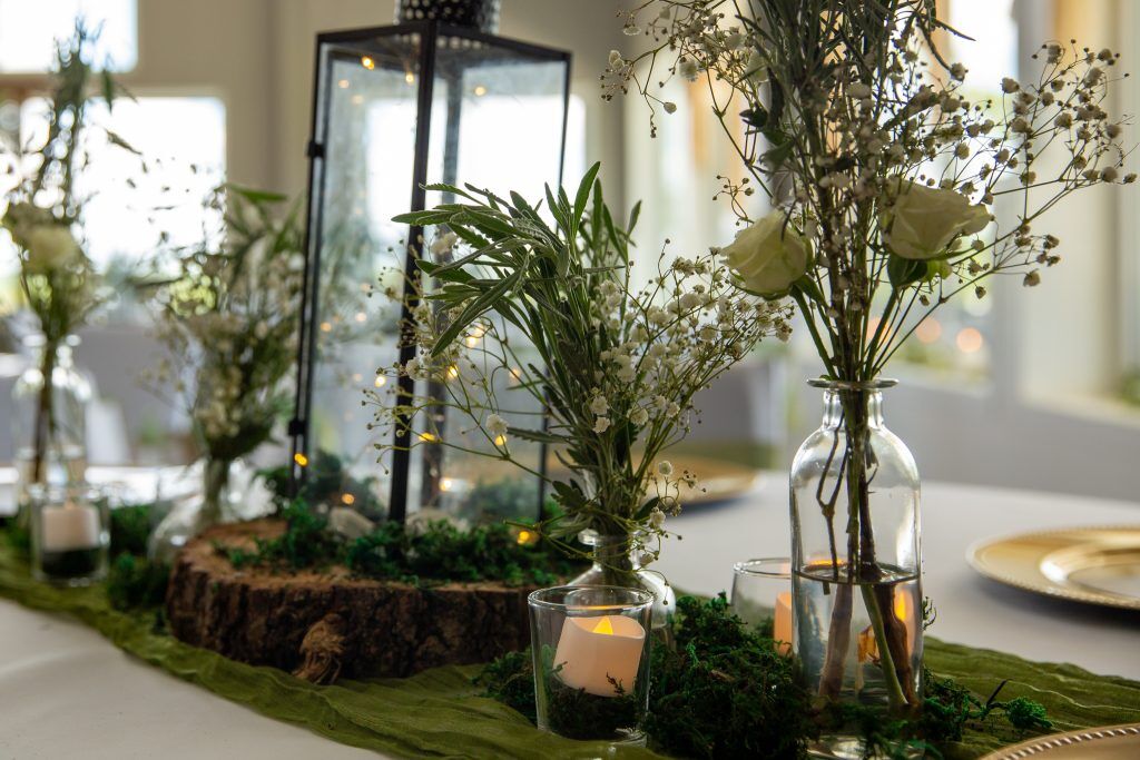 A beautiful table setting at a Venue near Tulsa with earthy green bouquets and wood and green sash with candles